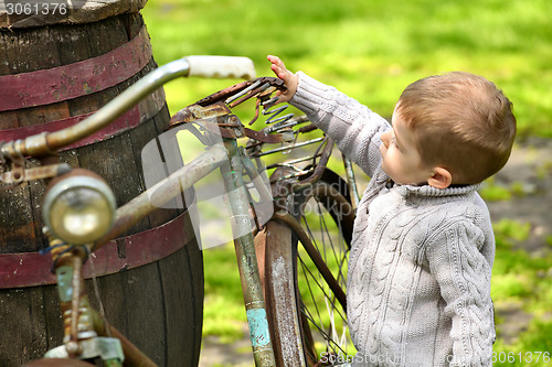 Image of 2 years old curious boy walking around the old bike 