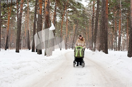 Image of Young mother with baby carriage in winter forest