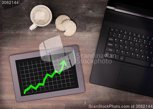 Image of Tablet touch computer gadget on wooden table, graph positive