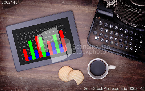 Image of Tablet touch computer gadget on wooden table, graph