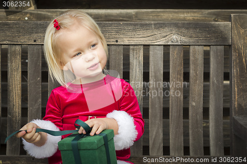 Image of Adorable Little Girl Unwrapping Her Gift on a Bench