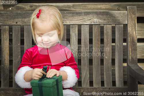 Image of Adorable Little Girl Unwrapping Her Gift on a Bench