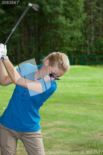 Image of Young woman golf player on course doing golf swing