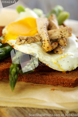 Image of Toast with egg, green asparagus and turkey on the old board..