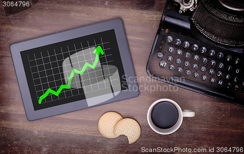 Image of Tablet touch computer gadget on wooden table, graph positive