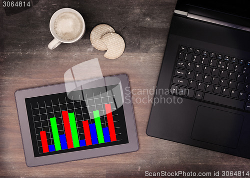 Image of Tablet touch computer gadget on wooden table, graph