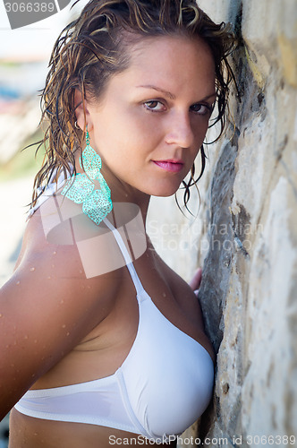 Image of Beautiful girl in bikini  stands near the stone wall