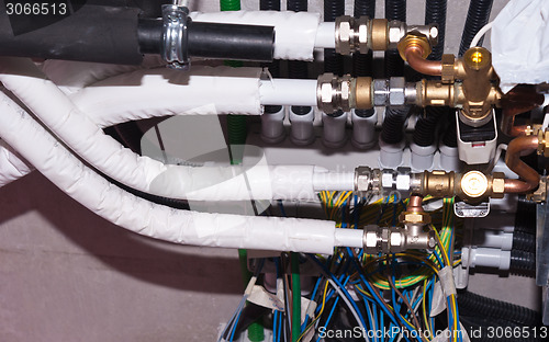 Image of white pipes brass nozzles valves and multicolored wires in indus