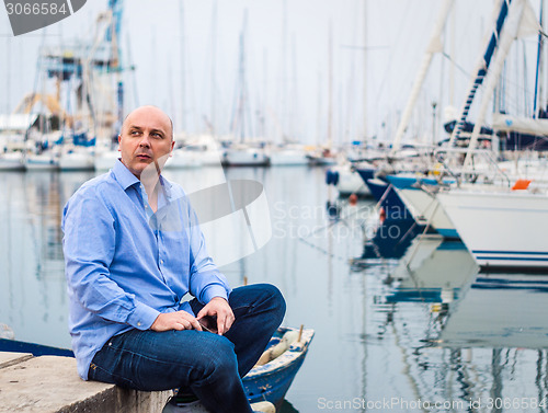 Image of Businessman sitting by expensive sailing boats and yachts in a c