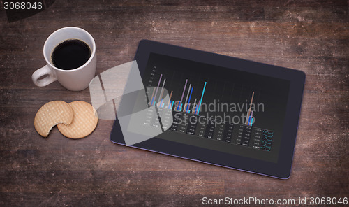 Image of Tablet touch computer gadget on wooden table, graph