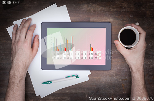 Image of Tablet touch computer gadget on wooden table, graph