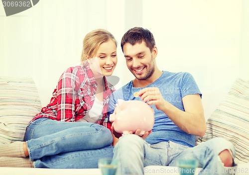 Image of smiling couple with piggybank sitting on sofa