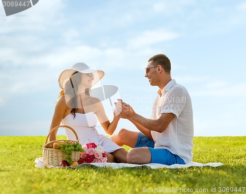 Image of smiling couple with small red gift box on picnic