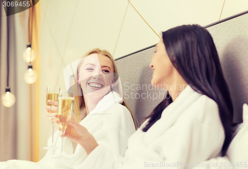 Image of smiling girlfriends with champagne glasses in bed