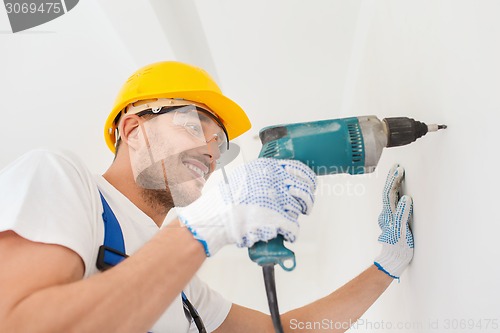 Image of smiling builder in hardhat drilling wall indoors