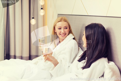 Image of smiling girlfriends with champagne glasses in bed