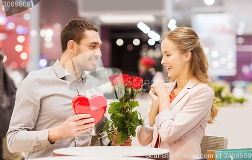 Image of happy couple with present and flowers in mall