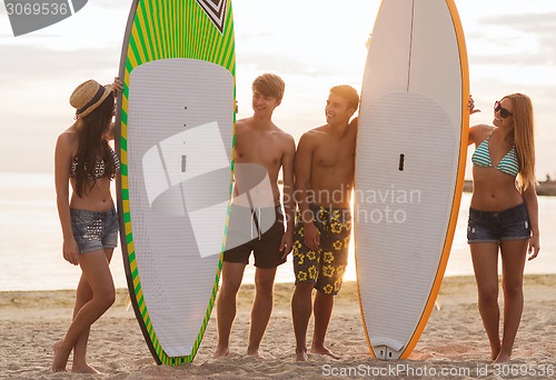 Image of smiling friends in sunglasses with surfs on beach