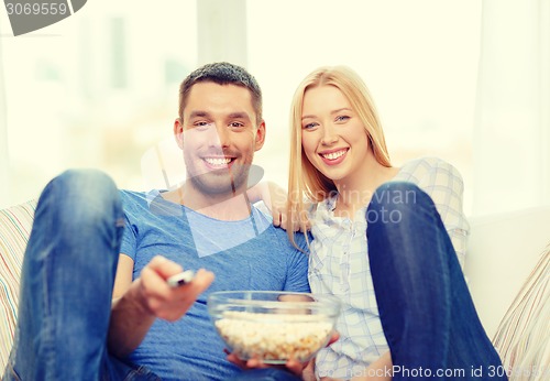 Image of smiling couple with popcorn watching movie at home