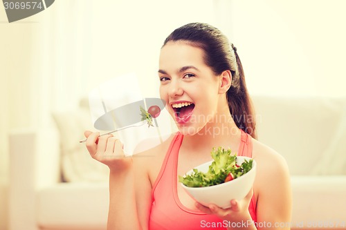 Image of smiling teenage girl with green salad at home