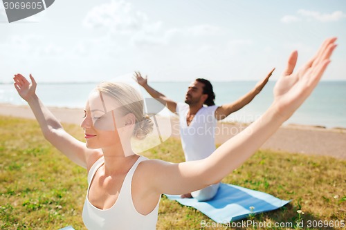 Image of smiling couple making yoga exercises outdoors