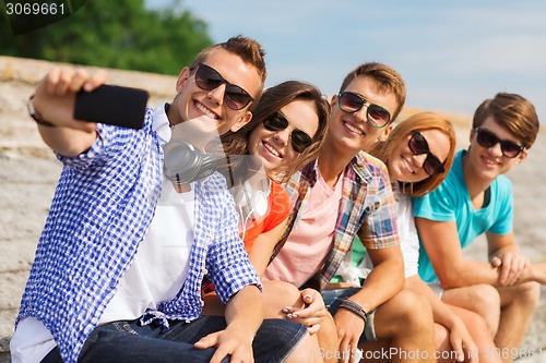 Image of group of smiling friends with smartphone outdoors