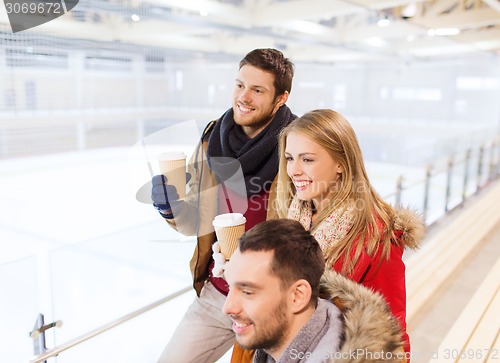 Image of happy friends with coffee cups on skating rink