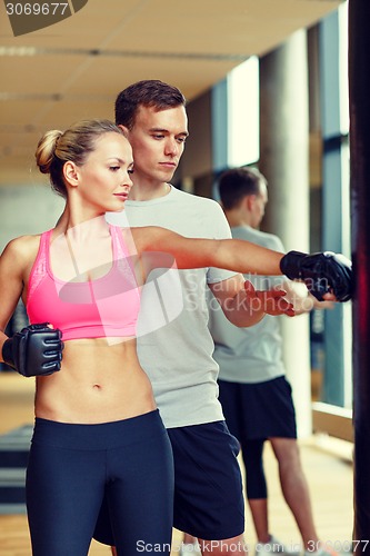 Image of smiling woman with personal trainer boxing in gym