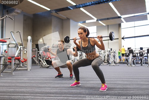 Image of young man and woman training with barbell in gym