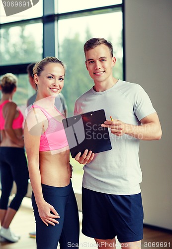 Image of smiling young woman with personal trainer in gym