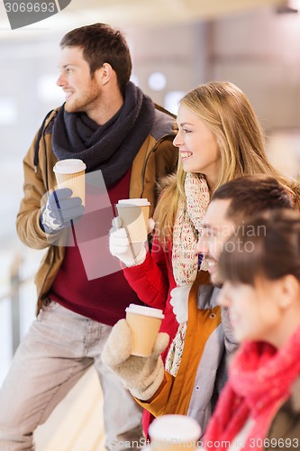 Image of happy friends with coffee cups on skating rink