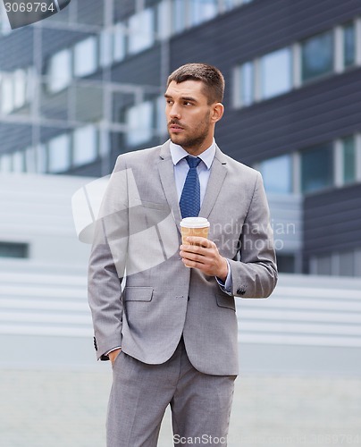 Image of young serious businessman with paper cup outdoors