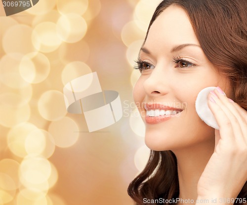 Image of smiling woman cleaning face skin with cotton pad