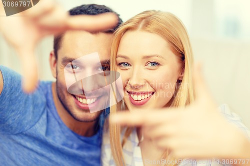 Image of smiling happy couple making frame gesture at home