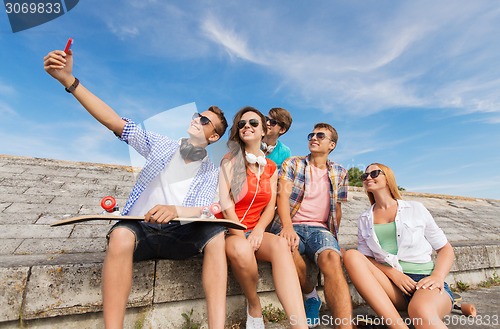 Image of group of smiling friends with smartphone outdoors