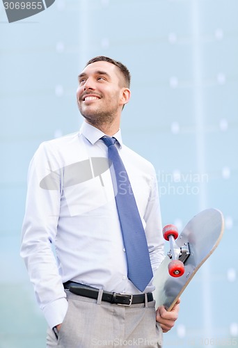 Image of young smiling businessman with skateboard outdoors