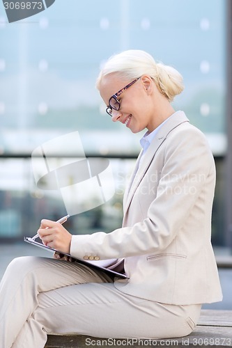 Image of young smiling businesswoman with notepad outdoors