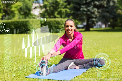 Image of smiling woman stretching leg on mat outdoors