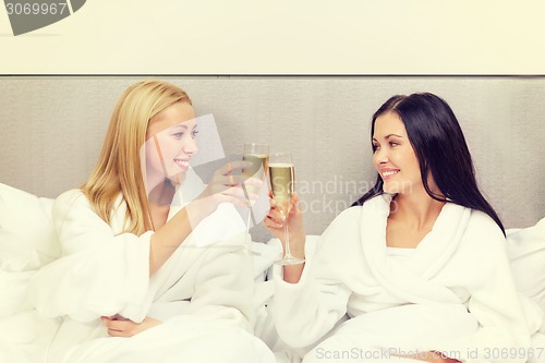 Image of smiling girlfriends with champagne glasses in bed