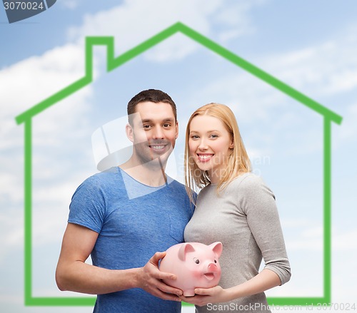 Image of smiling couple holding piggy bank over green house
