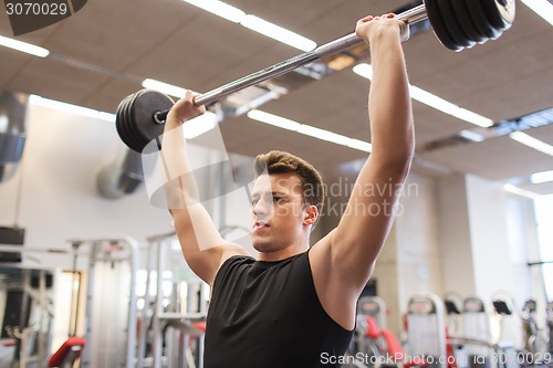 Image of young man flexing muscles with barbell in gym