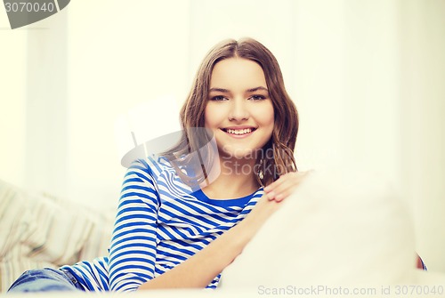 Image of smiling teenage girl sitting on sofa at home