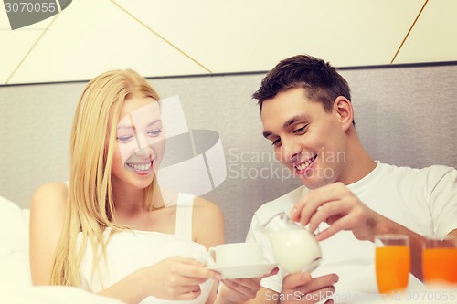 Image of smiling couple having breakfast in bed in hotel