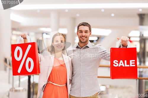 Image of happy young couple with red shopping bags in mall