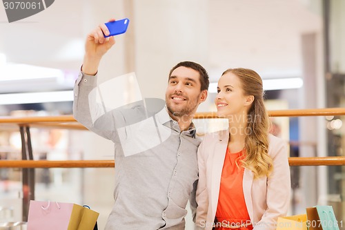 Image of happy couple with smartphone taking selfie in mall