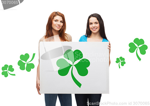 Image of smiling teenage girls holding board with shamrock