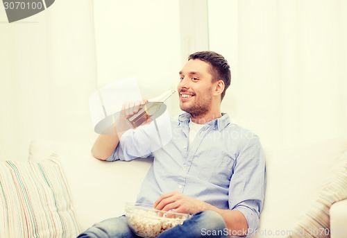 Image of smiling man with beer and popcorn at home