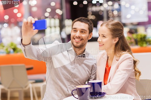 Image of happy couple with smartphone taking selfie in mall