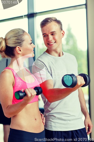 Image of smiling young woman with personal trainer in gym