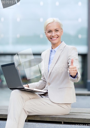 Image of smiling businesswoman working with laptop outdoors